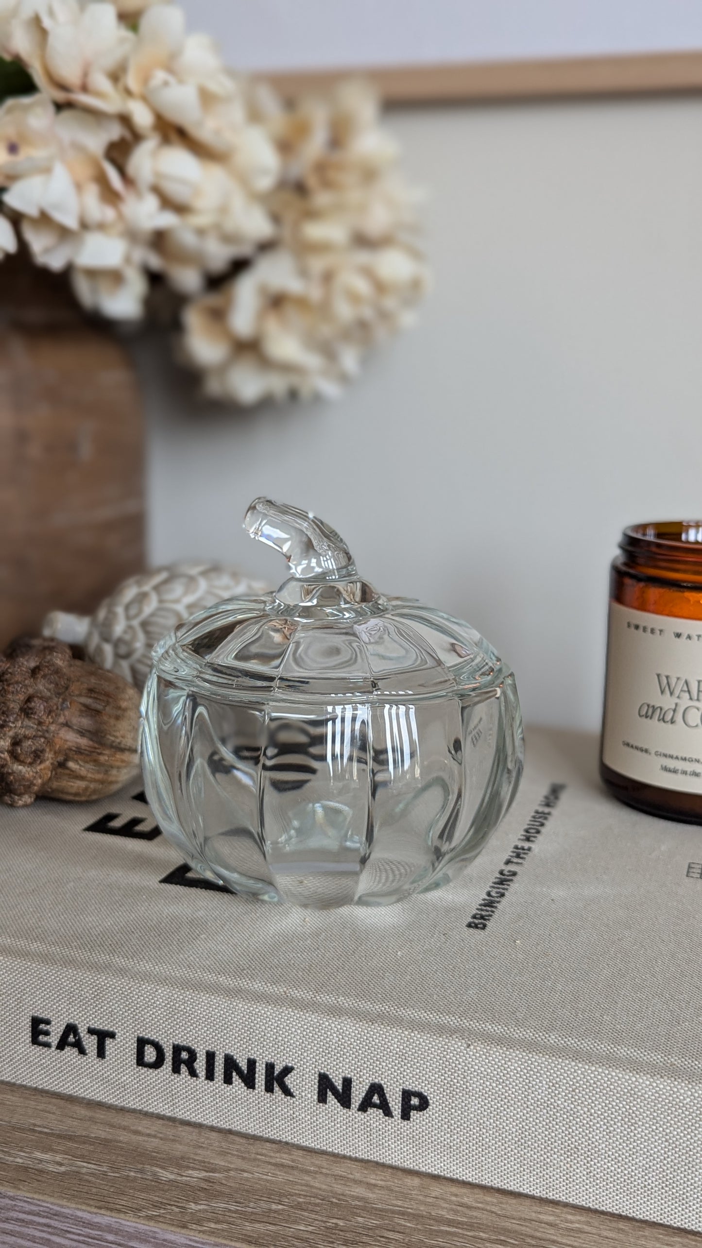 a lass lidded jar in the shape of a pumpkin sits among a host of rustic seasonal decor