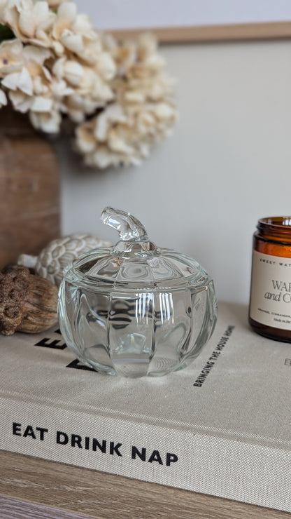 a lass lidded jar in the shape of a pumpkin sits among a host of rustic seasonal decor