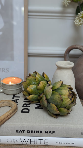 a pair of realistic green artichoke ornaments sit atop a decorative book stack t create a rustic cosy home coffee table display