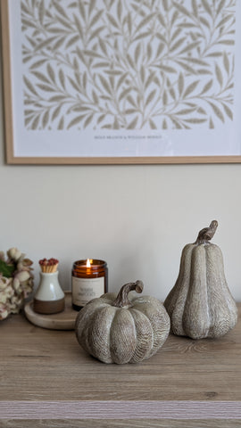 a rustic, wooden effect squat pumpkin sits in front of a taller matching wooden effect pumpkin to crate a cosy autumn display in warm colours and textures